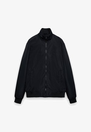 Giacca bomber nera in nylon con collo alto, davanti con cerniera, polsini elastici e tasche laterali. Texture liscia, design minimalista.