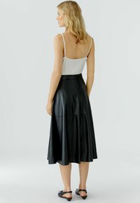 Schwarzer Leder-Midirock mit ausgestelltem Design, glatter Textur und taillierter Passform. Tragen mit einem weißen Trägershirt und schwarzen Ballerinas.