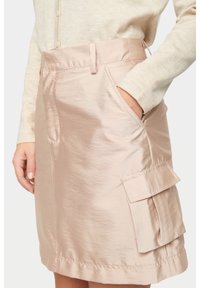 Ljusrosa kjol gjord av glänsande, slätt tyg med hög midja, sidofickor och två fickor i cargostil med ficklock.