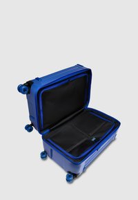 Blauer Hartschalenkoffer mit geripptem Design, vier drehbaren Rollen und Reißverschlussverschluss. Innen verfügt er über schwarze Netzfächer zur Organisation.