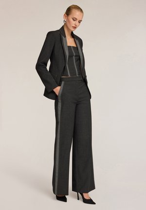 Completo nero caratterizzato da un blazer su misura con rever in satin, abbinato a un top cropped coordinato e pantaloni larghi con strisce laterali a contrasto.