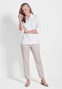 Weißes Hemd mit aufgerollten Ärmeln, kombiniert mit grauen gemusterten Slim-Fit-Hosen und beigen Ballerinas. Einfache, klare Linien und subtile Texturen.