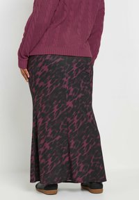 Un pull en mélange de laine de couleur violette avec un motif en cable, associé à une jupe noire ornée d'un motif abstrait violet, complété par des chaussures plates noires.