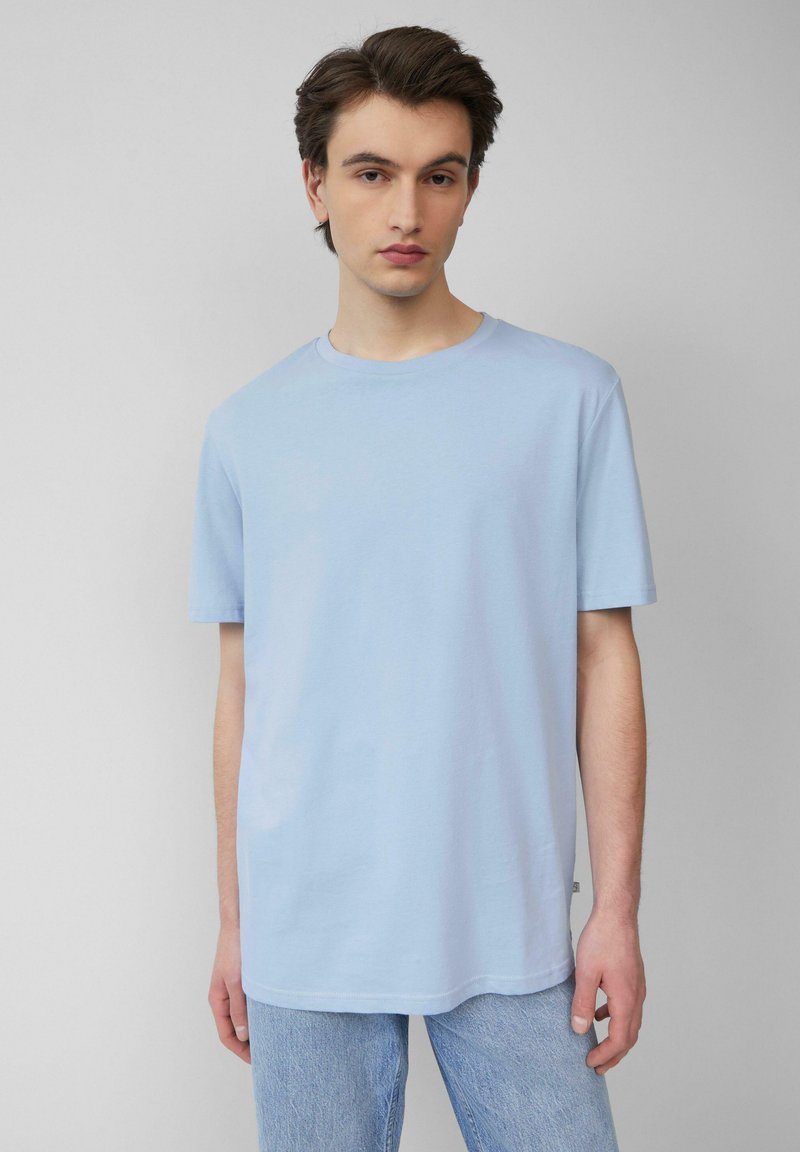 Lichtblauw, kort shirt met korte mouwen van zachte katoen. Ronde hals, ontspannen pasvorm, met rechte zoom. Gecombineerd met lichtblauwe spijkerbroek.