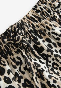 Tissu en imprimé léopard avec un fond beige neutre et de gros points noirs. Présente une taille élastique avec un accent noué. Texture douce.