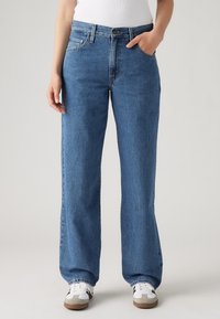 Lichtblauwe denim jeans met een ontspannen pasvorm, hoge taille, vijf zakken en een licht vervaagde textuur. Gepaard met witte en grijze sneakers.