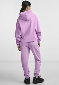 Felpa con cappuccio di colore viola chiaro e pantaloni della tuta abbinati, realizzati in un tessuto morbido; vestibilità rilassata con polsini e orli a costine; indossati con sneakers nere chunky.