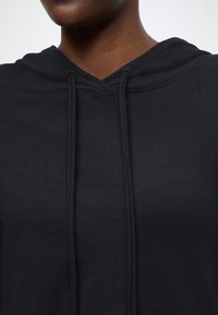 Μαύρο φούτερ με λαιμόκοψη σε σχήμα V, κορδόνια και απαλή υφή, εμφανιζόμενο από το στήθος και πάνω σε απλό λευκό φόντο.