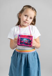 Pochette a tracolla colorata con design di fenicottero, dettagli in rosa e chiusura con zip, tenuta da un bambino in una gonna di jeans.