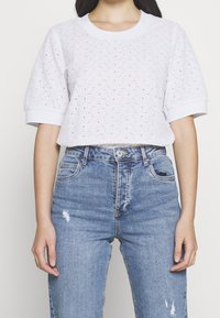 Top bianco a maniche corte con un design ad occhio di pernice testurizzato e polsini a costine, abbinato a jeans blu strappati a vita alta.