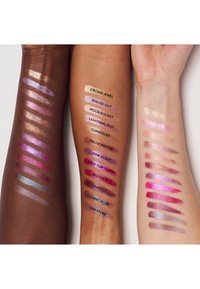 Tre arme viser forskellige makeup-swatcher i metalliske og matte finishes. Farverne spænder fra guld, pink og lilla til dyb brun.