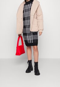 Giacca puffer beige, vestito lavorato a maglia a quadri bianco e nero, borsa rossa e stivali neri con lacci e suola spessa.