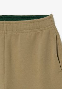 Tan joggers i tyg med texturerad yta, med ett grönt elastiskt midjeband och sidfickor.