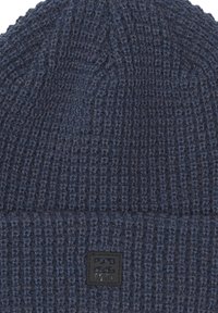 Gorro de lana en azul oscuro con un diseño texturizado. Cuenta con un parche de logo negro en el puño doblado para la marca.