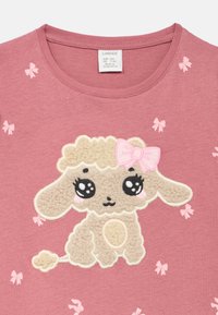 Rosa T-skjorte med korte ermer, mykt, brodert sauemotiv og små rosa sløyfeaksenter. Har rund hals.