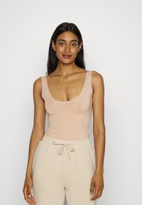 Nude top na ramiączkach z okrągłym dekoltem i grubymi ramiączkami, w połączeniu z jasnobeżowymi spodniami ze sznurkiem, obie części z gładkiego, miękkiego materiału.