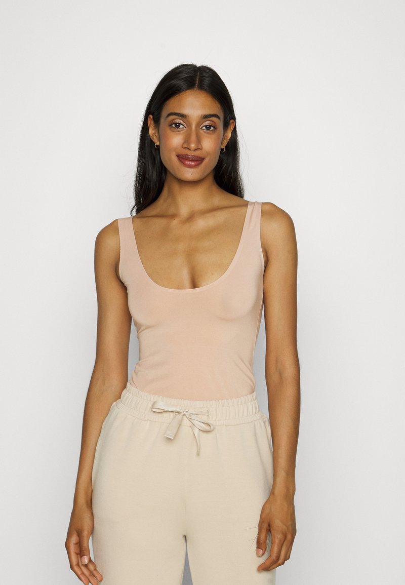 Nude top na ramiączkach z okrągłym dekoltem i grubymi ramiączkami, w połączeniu z jasnobeżowymi spodniami ze sznurkiem, obie części z gładkiego, miękkiego materiału.