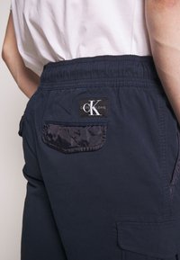 Pantalon cargo bleu marine avec taille élastique, doté d'une poche plaquée à l'arrière et d'une étiquette logo indiquant "Calvin Klein Jeans".