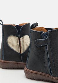 Bottes en cuir bleu marine avec un accent en or en forme de cœur et des coutures bleues contrastantes. Fermeture éclair sur le côté et semelle en caoutchouc texturée.