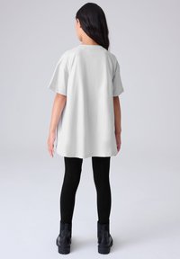 Svijetlosiva prevelika majica s okruglim izrezom, kratkim rukavima i bočnim prorezima, uparena s crnim tajicama i crnim gležnjačama.