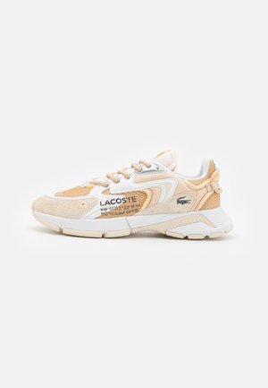 Beige og hvide Lacoste-sneakers med mesh, ruskindspaneler, mærket tekst og gummisål på hvid baggrund.