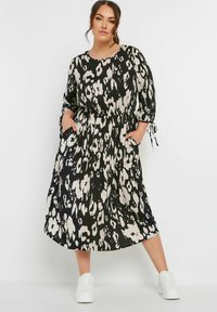 Klänning med leopardmönster i svart och krämfärg, lös passform, midja med dragsko, trekvartslånga ärmar och sidofickor. Styla med vita sneakers.