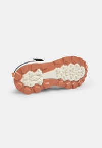 Suela de zapatilla de trail con un diseño robusto, con tacos de tracción prominentes, una base de color crema claro con acentos naranjas y una superficie texturizada.