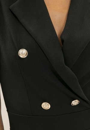 Blazer noir confectionné sur mesure avec de larges revers et quatre boutons dorés décoratifs à l'avant.