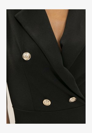Blazer noir confectionné sur mesure avec de larges revers et quatre boutons dorés décoratifs à l'avant.