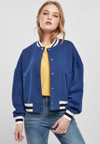 Blue bomber jacket with a relaxed fit, white and black striped ribbed cuffs and waistband, snap front closures, and side pockets.