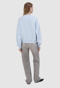 Jasnoniebieska bluza o luźnym, oversize’owym kroju, z prążkowanymi ściągaczami przy mankietach i dolnym brzegu, w zestawieniu z szerokimi, jasnoszarymi dżinsami. Prosty design, codzienny wygląd.