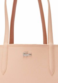 Borsa tote di un rosa chiaro con una finitura testurizzata, dotata di due manici in pelle marrone e di un accento con il logo del coccodrillo Lacoste in argento.