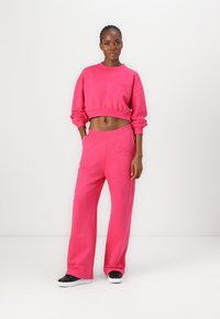 Pink cropped sweatshirt and matching sweatpants, both in a soft, textured fabric. The pants feature an embroidered logo on the side.