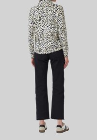 Blouse à manches longues avec une base crème ornée de taches de léopard noires et brunes, associée à un jean noir coupe droite et des baskets blanches.