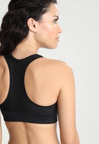Crna sportska bralette s teksturiranim dizajnom, u racerback stilu i elastičnom trakicom. Glatka tkanina i minimalistički izgled, pogodna za sportsku upotrebu.