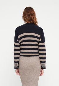 Námořnická a béžová pruhovaná pletená cardigan s cropped designem a dlouhými rukávy. Texturovaná tkanina se žebrovanými akcenty na ramenou a manžetách.