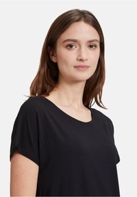 Top nero a maniche corte con scollatura ampia, realizzato in un tessuto morbido. Il design è semplice, senza fantasie o dettagli metallici.