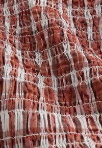 Tissu à carreaux rouille et blanc avec fronces élastiques réunies créant une surface texturée et plissée.