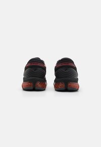Black athletic shoes with a textured design, featuring a maroon sole and prominent branding on the heel. Smooth fabric upper for comfort.