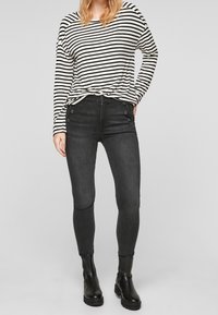 Černé skinny džíny z denimu s knoflíkovými detaily, v kombinaci s dlouhým rukávem černobílého pruhovaného topu. Hladká textura, přiléhavý střih.