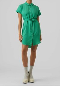 Grön kortärmad knapp-up klänning med krage, bälte i midjan och något längre baktill. Slät tyg med en mjuk textur.