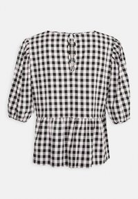 Blouse à carreaux vichy noir et blanc avec des manches bouffantes, un ourlet à basque et une ouverture en forme de goutte d'eau au dos. Le tissu a une finition texturée.