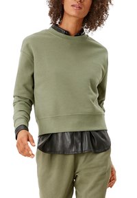 Felpa verde oliva chiaro con scollatura rotonda e maniche lunghe, sovrapposta a una camicia in pelle nera. Tessuto morbido, design corto.