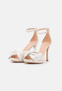 White satin high-heeled shoes with a front knot detail, ankle strap, open toe, and a smooth finish. Features a slender stiletto heel.