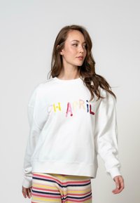 Fehér pulóver, amelyen színes, bolyhos betűk formájában az "OH APRIL" felirat látható. Puha anyag, ejtett vállakkal és bordázott mandzsettákkal. Csíkos alj.