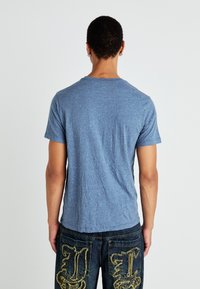 Μπλε κοντομάνικο μπλουζάκι φτιαγμένο από μαλακό ύφασμα με χαλαρή εφαρμογή. Η ελαφριά υφή και ο άνετος σχεδιασμός είναι ορατά από την πίσω όψη.