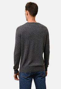 Grauer Rundhalspullover aus Strickstoff. Mit langen Ärmeln und einem gerippten Saum. Kombiniert mit dunkelblauen Jeans.