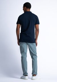 Námořnická polo košile, krátké rukávy, volný střih. Světle tyrkysové kalhoty, slim fit, ohrnuté nohavice. Bílé tenisky se zeleným akcentem. Jednoduché pozadí.