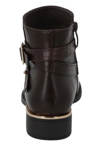 Botín de cuero marrón que presenta una correa texturizada, un acento dorado y un tacón apilado con un acabado mate. La vista trasera muestra un diseño elegante.