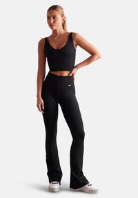 Black ribbed crop top and matching high-waisted flared leggings. Material appears stretchy. White footwear with black accents completes the outfit.